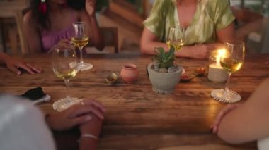 Garson gün batımında atmosferik açık hava restoranında çeşitli bayan arkadaşların masasına mum koyuyor. Alacakaranlıkta tropikal kafede konuşan ve gülümseyen çok ırklı kızlar. Genç çoklu etnik kadınlar akşam yemeği