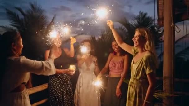 クリスマスパーティーで燃える輝きで踊る多様な女性 若い多人種の女性は手に輝くライトと独立記念日のお祝いの夕食中に楽しみを持っています 誕生日 — ストック動画