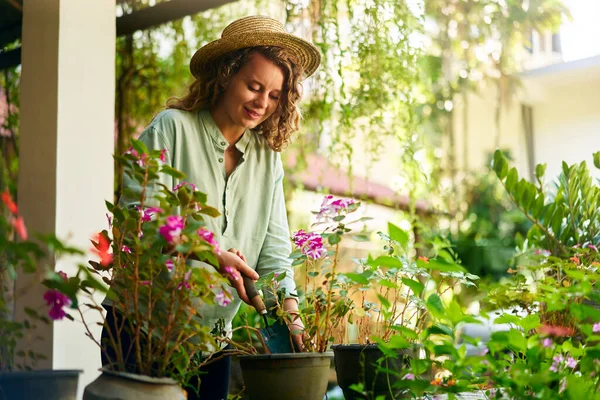 戴着草帽的年轻女园丁拿着铲子照料盆栽 年轻的高加索女人笑着站在她的花园里 在盆子里种花 园艺和耕作概念 图库照片