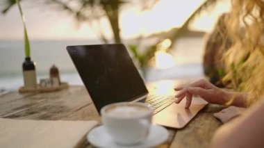 Bilgisayardaki kadın kripto para tüccarı günbatımında açık deniz kafesinde çalışan online haritaları kontrol ediyor. Kadın kripto komisyoncusu okyanusa yakın plandaki borsa oranlarının grafiklerini analiz ediyor.