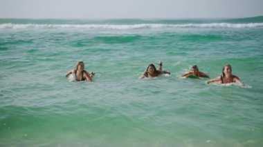 Genç çok ırklı kadın sörfçüler gün doğumunda tropik plajda denize doğru sörf tahtaları üzerinde kürek çekiyorlar. Kız arkadaşlar yaz tatili şafağında açık hava yaşam tarzını ve su sporlarını severler..