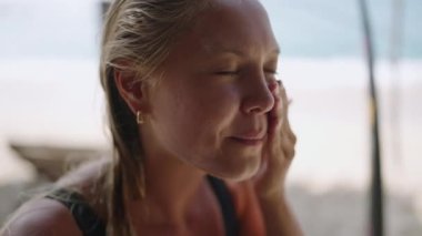 Sarışın beyaz kadın sörfçü yüzüne güneş kremi sürüyor. Bronzlaşmış genç sörfçü kadın yanaklarına, burnuna ve alnına yakın çekim yapıyor. Sörfçü bir kızın portresi cilt koruması kullanıyor.