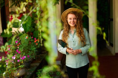 Hasır şapkalı genç kadın bahçıvan bahçede durmuş mutlu bir şekilde gülümseyen kameraya bakıyor. Arka planda yeşil meyve bahçesi olan neşeli beyaz kadın. Bahçıvanlık ve tarım kavramı.