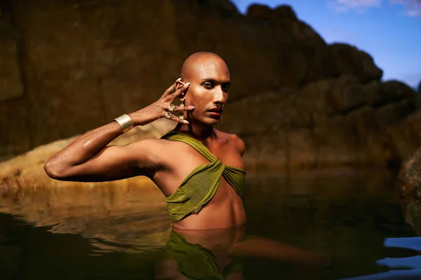 stock image Non-binary person of color poses in water, shows jewelry inside scenic creek at night. Lgbtq ethnic graceful fashion model wear brass rings with gems, nose-ring, earrings, bracelets immersed in pond.