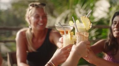 Çok ırklı kadınlar tezahürat yapıyor ve bardaklarını tokuşturarak açık bir kafede kokteyl partisinden zevk alıyorlar. Bir grup etnik çeşitlilikte kadın arkadaş tropikal bir çatı katında kokteyl içip eğleniyorlar..