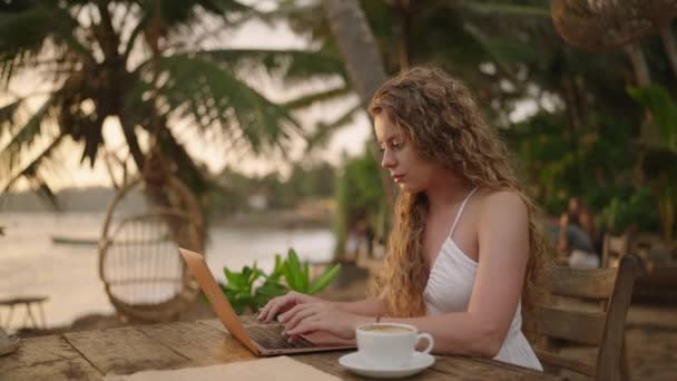 年轻的女开发人员在笔记本电脑上工作 在海洋边创建应用程序 室外热带咖啡店的女自由撰稿人 白人女孩在异国他乡工作全球工作概念 — 图库视频影像