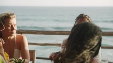 Brunch 'ta deniz manzaralı bir restoranda çok ırklı bayan arkadaşlar sohbet edip kokteyl içiyorlar. Tropikal okyanus manzaralı kahkahalar ve yudumlanmış içecekler masasında oturan çok ırklı ve neşeli kızlar.