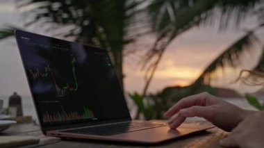 Bilgisayardaki kadın kripto para tüccarı günbatımında açık deniz kafesinde çalışan online haritaları kontrol ediyor. Kadın kripto komisyoncusu okyanusa yakın plandaki borsa oranlarının grafiklerini analiz ediyor.
