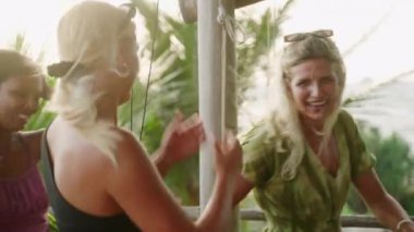 Açık terasta çeşitli dişiler, rüzgar saçlarını savuruyor. Gün batımında, açık hava restoranındaki akşam yemeği partisinde çok ırklı, neşeli genç kadınlar havada uçuşan saçlarla. Gülen çok kültürlü kızlar.