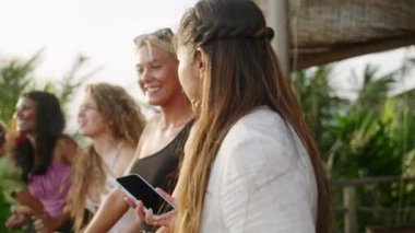 Neşeli çok ırklı kızlar tatilde selfie çeker. Çeşitli genç dişiler akıllı telefonla kendi portresini çekiyor. Çok ırklı mutlu kadın arkadaşlar gülümsüyor ve egzotik yerlerde gülüyorlar..
