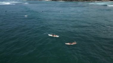 Genç bayan sörfçüler güneşli bir günde deniz manzaralı tropik bir yerde sörf tahtasında kürek çekiyorlar. Sörf yapan kızlar yaz tatilinde drone 'dan sörf ve su sporlarının keyfini çıkarıyorlar..