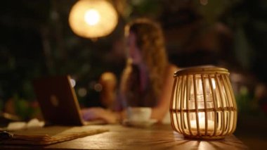 Kadın serbest yazar gece atmosferik açık hava tropikal mekanında çalışıyor. Dışarıdaki karanlık kafedeki masada oturan bir kadın sıcak ışıklar, saman ve dizüstü bilgisayar kullanan ahşap lambalarla. Geç saatlere kadar çalışıyorum
