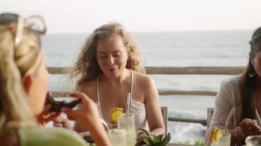 Çatal ve bıçakla deniz manzaralı çatı restoranında yemek yiyen bir kadın. Genç beyaz kadın arkadaşlarıyla otantik tropikal açık kafede vegan yiyecekler yiyor. Beyaz kız sağlıklı yemeğin tadını çıkarıyor..