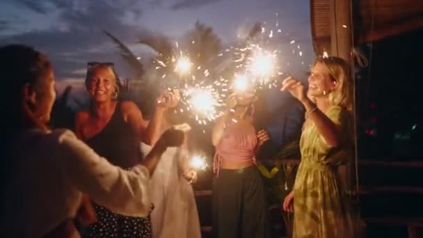 夕暮れ時の海辺のトロピカルヘンパーティーでは 様々な女性がキラキラと踊り笑います 若い笑顔の多人種の女性は輝くライトで海による独立記念日のお祝いで楽しんでいます — ストック動画