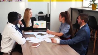 Business woman makes a presentation with charts, diagrams for multiethnic partners. Startup team discuss project plan. Diverse multinational people have meeting in office listening to a supervisor.