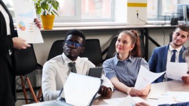 Business woman presents report, shows diagrams, charts in conference room for multiethnic partners. Diverse international team listen CEO on briefing meeting in office. Corporate people discuss plans.