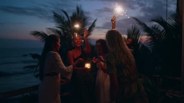 熱帯のお祝いパーティーで楽しい時間を過ごしている若い多人種の女性たちが輝くライトを手にしています パーティーで様々な女性の応援とダンスの保持と燃える輝きを振ってのグループ — ストック動画