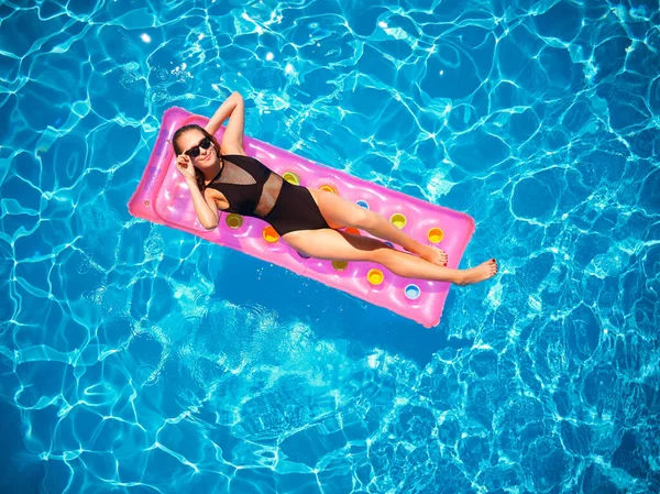 stock image Fit pretty girl in bikini chilling on inflatable pink mattress in swimming pool. Slim hot woman in swimwear tanning. Female relaxing on a float in blue water at luxury resort. Aerial, view from above.