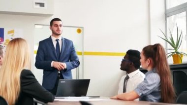 Businessman reporting to multiethnic partners audience in conference room. Diverse international team listen to CEO on meeting in office. Corporate people discuss business strategy on briefing.