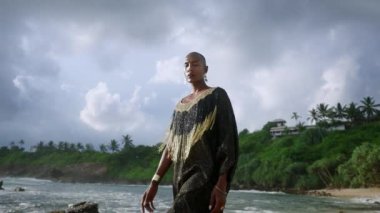 Lüks giysiler içinde cinsiyeti değişken bir insan, manzaralı dalgalı okyanus kıyısında mücevher yürüyüşleri. Şatafatlı zengin elbisesi içinde abartılı bir manken deniz feneri uçurumuyla kumsala gider. Huysuz gökyüzü.