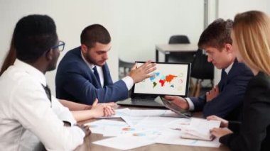 Businessman shows presentation with charts, diagrams on laptop for multiethnic partners. Startup team discuss project results. Diverse multinational people listening ceo on board meeting in an office.