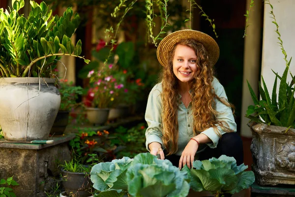 坐在菜园里种植蔬菜的年轻妇女微笑着看着摄像机 年轻的女园艺师在果园里用园艺工具照料蔬菜 耕作和园艺概念 — 图库照片