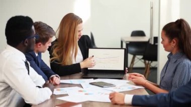 Business woman shows a presentation with charts, diagrams on laptop for multiethnic partners. Startup team discuss project plan. Diverse multinational people listening supervisor on meeting in office.