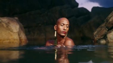 Androgynous siyah model, geceleri tropikal adada kayalarla çevrili doğal havuzun derinliklerinde bir sandık oluşturuyor. Durgun, egzotik manzaralı bir mekanın ortasında transseksüel etnik model.