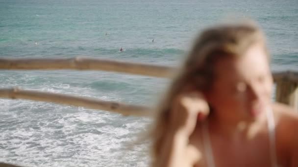冲浪者排队等待着完美的海浪 满脸笑容的金发年轻女子 一头卷曲的长发在海景屋顶热带咖啡馆与朋友们交谈 风吹来的头发漫不经心 海滨餐馆 — 图库视频影像
