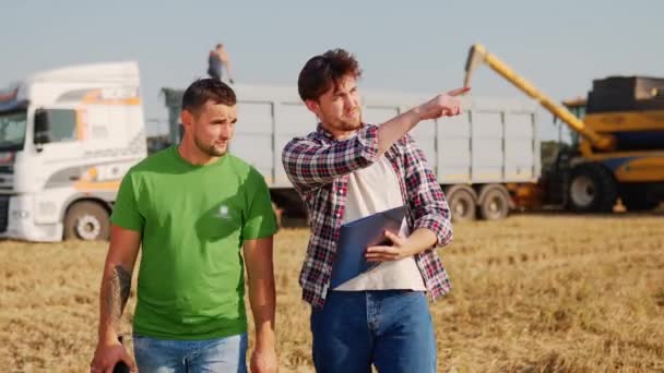 农民们在麦田里散步 讨论着 农艺师 物流代理与触控平板Pc谈判时 收割机装运谷物卡车 带有在线数据管理应用程序的精准耕作 — 图库视频影像