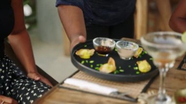 Tablada bronzlaşmış kadına yemek servisi yapan garson. Garson tabağı bir tepsiden nefis yiyeceklerle alıyor ve masaya yakın bir yere koyuyor. Kadın müşteriler için restoran masasına el yapımı gurme yemeği..