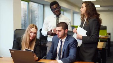 Diverse office corporate workers discuss project on laptop display in office. Multiethnic people planning startup strategy on meeting. Business team consulting on product design on a creative brief.