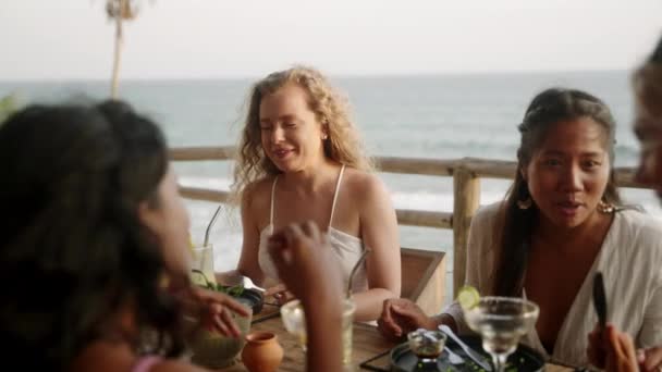 多様な人種の女性の友人が食事や会話をしながら食事をしている 幸せな多民族の女性のグループは レストランで食事やゴシップでプレートを交換します 休暇中の女の子のダイニングパーティー — ストック動画
