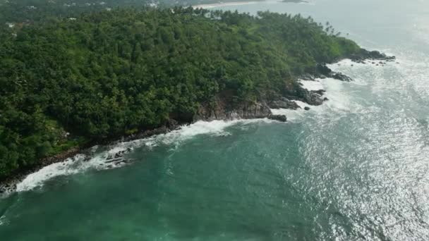 落基热带岛屿上覆盖着绿树成荫的植物 在大海的中央被海浪的空中景色冲刷着 汹涌大海环绕的悬崖峭壁上茂密的树叶 海浪冲击着岩石 — 图库视频影像