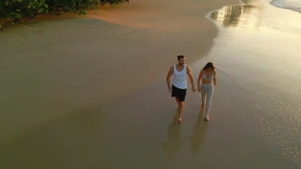 在日出前 情侣们手牵手沿着潮水在热带海滩上散步 俯瞰着大海 男朋友和女朋友在海边的沙滩上飞奔 在水边谈天说地 — 图库视频影像