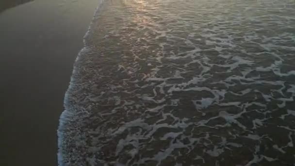 日の出に砂の上を走る波 若いカップルは 手空の景色を保持する潮に歩いています ボーイフレンドとガールフレンドが行く ドローンからの夜明けのバックビュー映像で海辺でビーチで話す — ストック動画