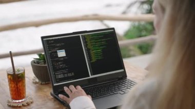 Tropikal kafede uzaktan çalışma gününde dizüstü bilgisayarı olan yumuşak dişi dev. Yazılım geliştiricisi günbatımında deniz manzaralı birlikte çalışan restoranda bilgisayar ekranına program kodu yazar. Okyanus kenarında kod yazan kadın.