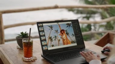 Görüntü düzenleme yazılımıyla çalışan kadın fotoğraf editörü. Seyahat fotoğrafçısı fotoğrafları düzenler. Retoucher serbest çalışan kadın bir tropik restoranda dizüstü bilgisayardaki resimlere renk düzeltmesi yapıyor..