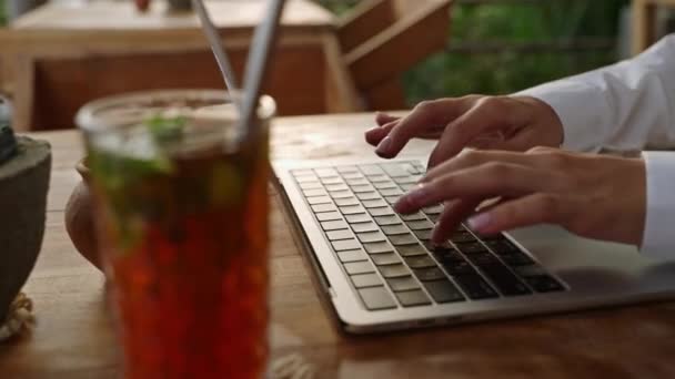 女人在咖啡店的笔记本电脑键盘上打字 作家创作了一首诗 人们在室外用笔记本电脑与冰茶 棕榈树一起创作电子邮件 记者撰写文章 博客写文章 — 图库视频影像