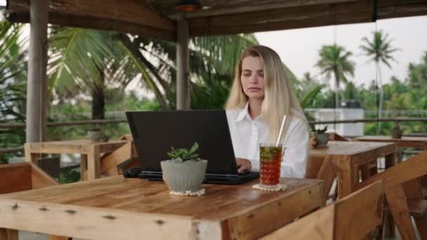 Egy Szőke Laptoppal Dolgozik Egy Pálmafákkal Teli Kávézóban Számítógépet Használ — Stock videók