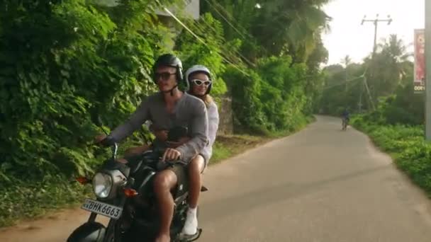 バイクで旅行する楽しい若いカップル 2人の陽気な恋人がジャングルロードでバイクに乗る ガールフレンドは笑い 波の手 旅行者は日没時にスクーターを運転する 女性のスクーターの冒険 — ストック動画