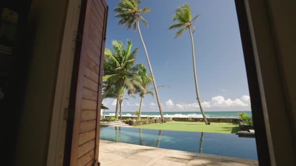 复古别墅客厅出口到后院 有游泳池和海滨 地平线 棕榈树景观 奢华的度假胜地 有蓝色的池塘 炎热的热带岛屿日光浴 — 图库视频影像