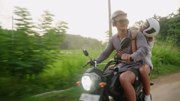 バイクに乗る素敵なカップル ライスプランテーションフィールドでバイクで旅行する愛好家 ガールフレンドが腕を広げる ジャングルでスクーターを運転する男 旅行者は自転車で島を探索する 冒険に女性 — ストック動画