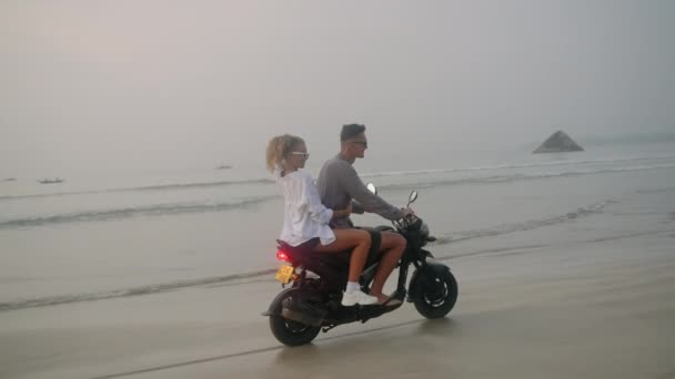 日落时 年轻人在海滩上骑摩托车 女人骑摩托车沿着海岸线漂洋过海女人们拥抱着男朋友 举起手来 抚摸着风中飘扬的头发 那家伙骑自行车 — 图库视频影像
