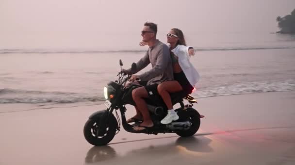 日落时分 这对旅行夫妇骑摩托车在热带天堂的沙滩上 男人与女友驾驶摩托车在海岸水边 女人喜欢和情人一起冒险 — 图库视频影像