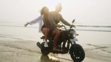 Mutlu insanlar gün doğumunda deniz kenarında motosikletle su sıçratırlar. Aşık çift okyanus kıyısında motosiklet sürerken eğleniyor. Kız erkek arkadaşını kucaklıyor, elini kaldırıyor. Güneş merceği parlamaları, yavaş çekim.
