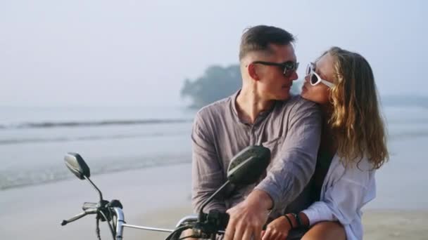 恋爱中的女人骑摩托车坐在海边 享受日落 女友拥抱 看男人在海上骑摩托车 新婚夫妇度蜜月 享受热带岛屿度假 — 图库视频影像