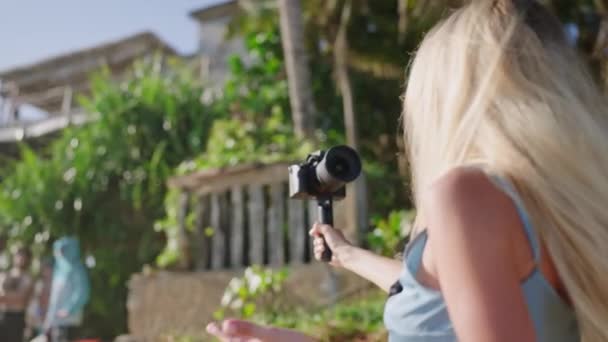 女性ブロガーが海のビーチでビデオを撮影 ブロンドの女性は熱帯島のプロカメラで歩くブログを撮影します インフルエンサーはソーシャルネットワークのストーリーを記録します Vloggerは旅行映画 バックビューで動作します — ストック動画
