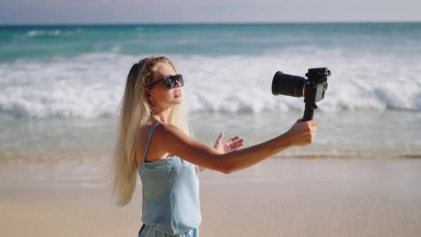 女性旅行爱好者喜欢在斯里兰卡的海滨度假 在镜头前拍摄自己 年轻的金发碧眼的博客作者戴着太阳镜站在沙滩上 手持专业的电影摄像机 慢动作 — 图库视频影像
