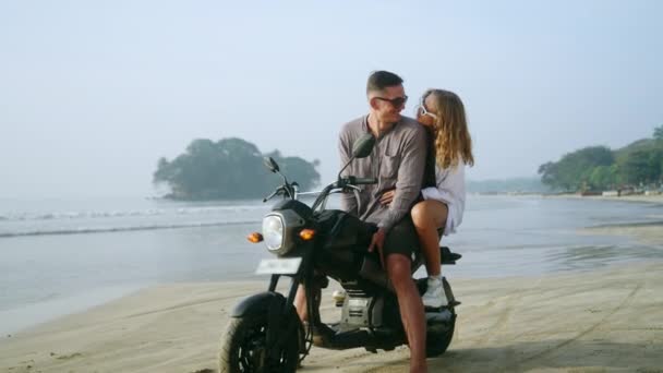 恋爱中的女人骑摩托车坐在海边 享受日落 女友拥抱 看男人在海上骑摩托车 新婚夫妇度蜜月时喜欢看照相机 — 图库视频影像